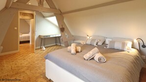 Un dormitorio con techo inclinado, una cama con almohadas y toallas enrolladas, un escritorio y una mesita.