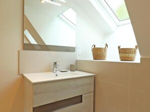 Une salle de bain moderne avec une lucarne, un grand miroir et deux paniers en osier posés sur le rebord de la fenêtre.