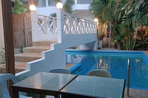 A pool area with a glass table and chairs, a wooden fence, and steps leading to a balcony. - Alona KatChaJo Inn (Panglao Municipality)