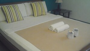 Una cama bien hecha con almohadas a rayas, una toalla enrollada y dos pequeños recipientes sobre un edredón color crema.