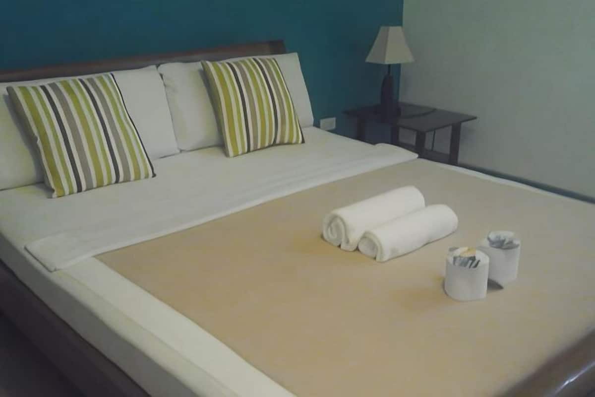 A neatly made bed with striped pillows, a rolled towel, and two small containers on a beige bedspread.