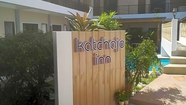 Un letrero de madera con la inscripción 'Katchajo inn', rodeado de vegetación y una zona de piscina.
