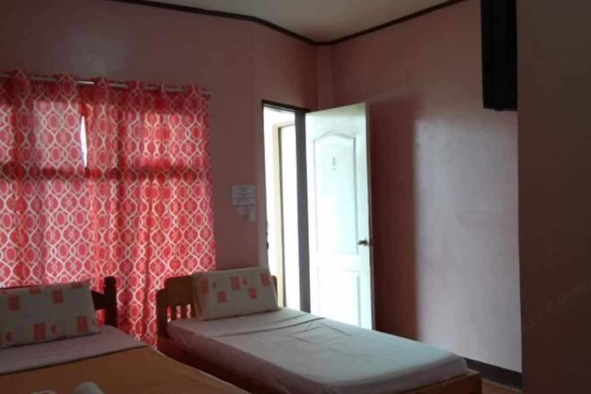 A bedroom with two beds, a window with patterned curtains, and a door.