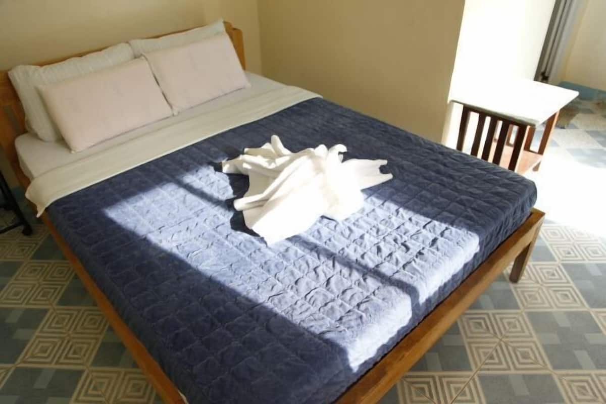 A bed with a blue quilt, a wooden frame, and a white pillow.