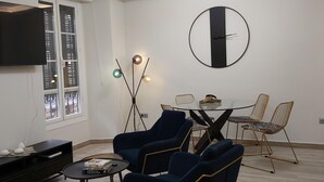 A modern living room with a flat-screen TV, a round table with chairs, and a large wall clock. - Malaga: Modern Apartment in Historic Center (Málaga)
