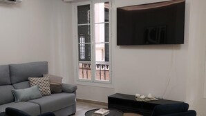 A modern living room with a grey sofa, two blue armchairs, a small coffee table, and a TV mounted on the wall. - Malaga: Modern Apartment in Historic Center (Málaga)