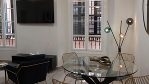 A modern living room with a glass dining table, zebra-striped chairs, a dark blue sofa, and a flat-screen TV mounted on the wall. - Malaga: Modern Apartment in Historic Center (Málaga)