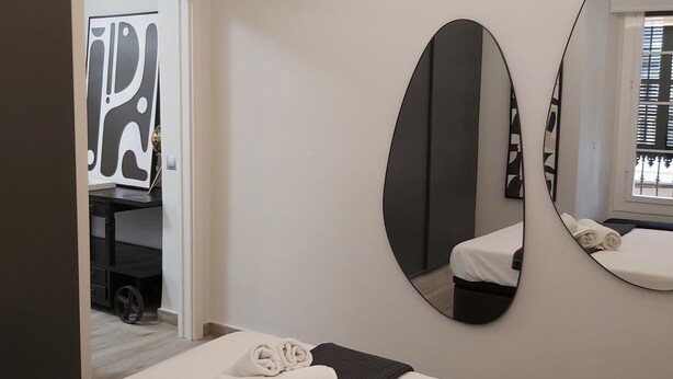 A hotel room with a bed, a large oval mirror, and a door with a modern design. - Malaga: Modern Apartment in Historic Center (Málaga)