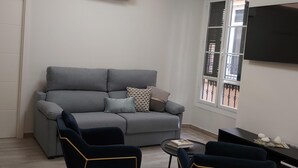 A modern living room with a grey sofa, two armchairs, a small coffee table, and a flat-screen TV mounted on the wall. - Malaga: Modern Apartment in Historic Center (Málaga)