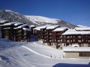 A snow-covered mountain with a ski resort building featuring multiple balconies and a ski slope in the foreground.