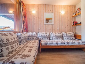 Una sala de estar acogedora con una pared de madera, un sofá con cojines estampados, una mesa de centro de madera y una estantería llena de libros.