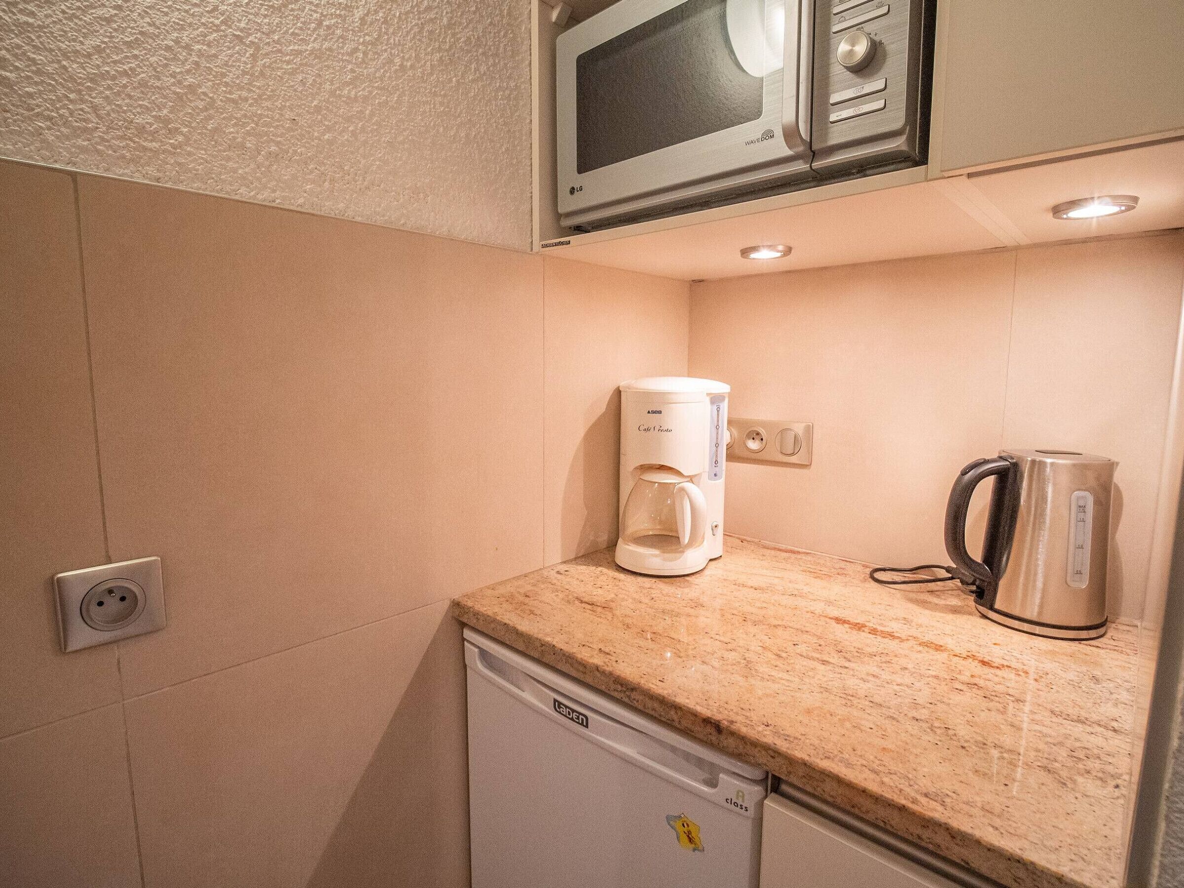 A compact kitchenette with a microwave, a coffee maker, and a kettle on the countertop.
