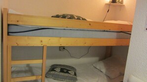 A bunk bed with a wooden frame, a pillow with a patterned design, and a wall socket.