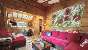 A cozy log cabin interior with a dining area, a red sofa, and a large floral painting on the wall.