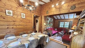 A wooden cabin with a dining area, a living room with a sofa, and a large window.