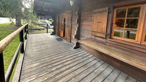 A wooden cabin with a wooden deck, large windows, and a door.