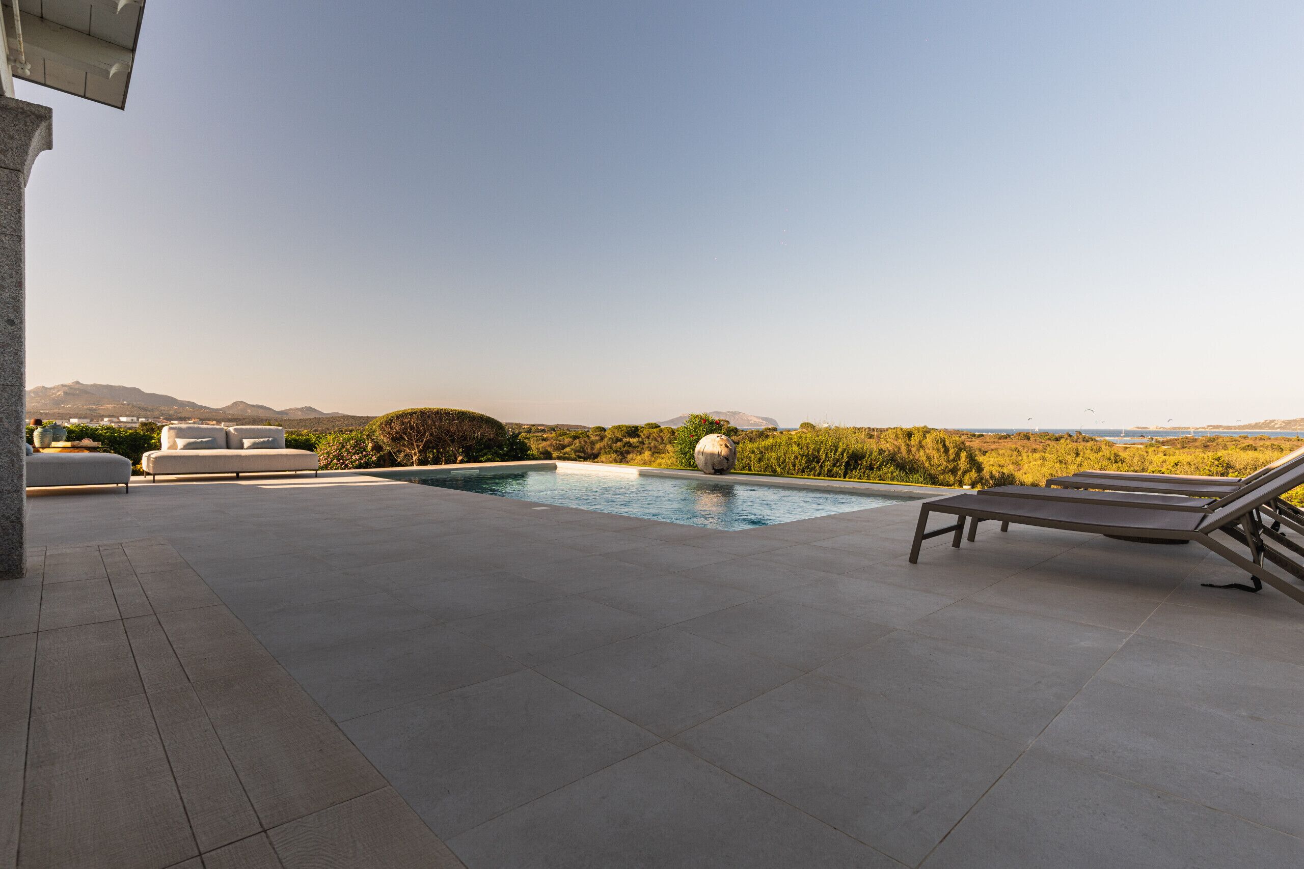 A rooftop pool area with a clear view of the mountains, a lounge chair, and a modern outdoor seating area.