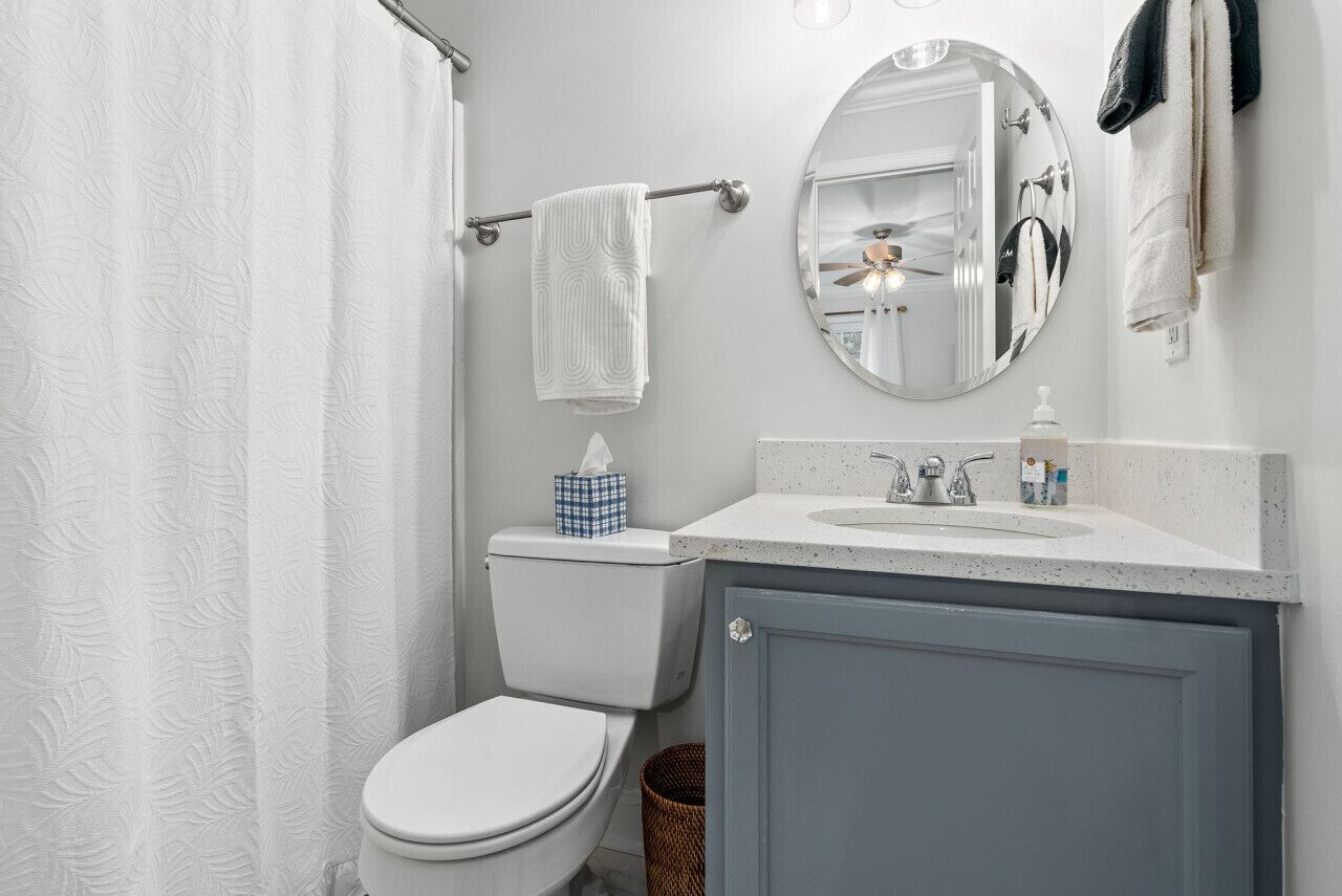 A bathroom with a toilet, a sink, a mirror, and a shower curtain.