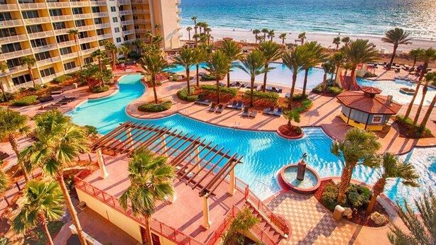 Un complexe hôtelier doté d’une grande piscine, de palmiers et offrant une vue sur la plage.