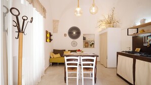 Un comedor con mesa y sillas, una zona de cocina con estufa, y una sala de estar con sofá y cojines.