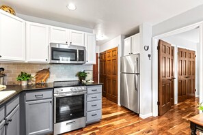 Une cuisine moderne avec des armoires blanches, des appareils en acier inoxydable et un plancher en bois.