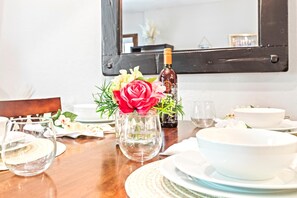 Une table à manger dressée avec de l’assiette, des bols et des verres blancs, une bouteille de vin et un vase rempli de fleurs.