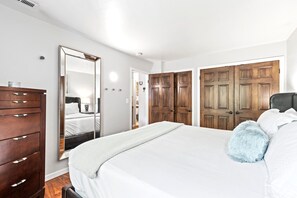 Une chambre à coucher avec un grand lit, une commode, un miroir et une porte double en bois.
