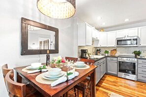Eine moderne Küche mit weißen Schränken, einem Edelstahlbackofen und einem Essbereich mit Holztisch und -stühlen.