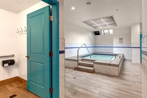 Eine türkisblaue Tür führt zu einem Badezimmer mit Badewanne, Handläufer und einem Notrufschild für die 911.