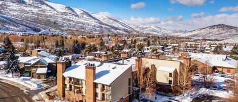 A town with snow-covered buildings, a road, and mountains in the background.