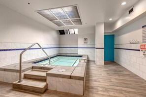 Un espace autour d’une piscine, avec des marches menant à l’intérieur de la piscine, un luminaire au plafond et une porte visible au fond.