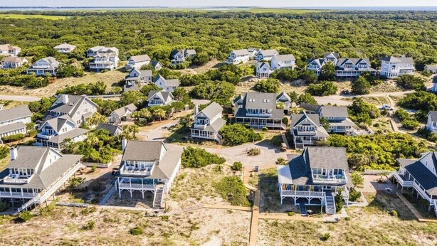 A coastal residential area with multiple houses, some with large porches and others with attached garages. - "Bleu Fin Cottage" BHI Club, Ocean Front, Steps to Beach, Sleeps 6 (Bald Head Island)