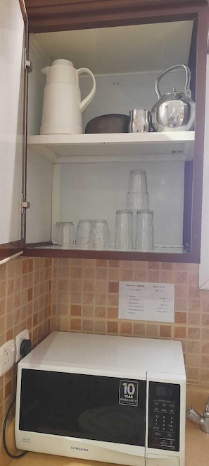 A kitchen with a microwave, a cabinet with dishes, and a sign listing available services. - luluh elthurayaa (Riyadh)