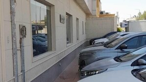 A parking area with several cars parked in front of a building with large windows and a tiled facade. - luluh elthurayaa (Riyadh)