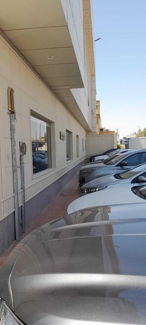 A parking area with several cars parked in front of a building with large windows and a tiled facade. - luluh elthurayaa (Riyadh)