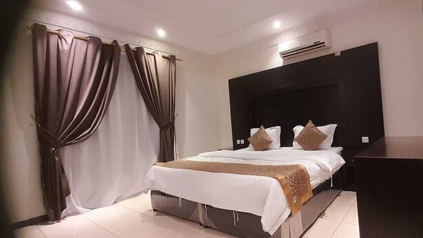 A hotel room with a large bed, dark headboard, and curtains. - luluh elthurayaa (Riyadh)