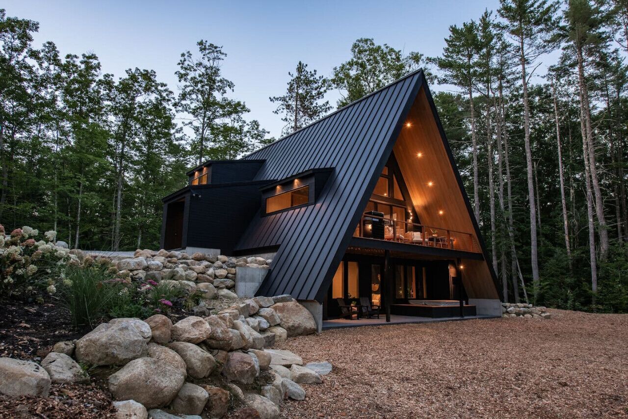Eine moderne, dreieckig-dachige Holzhütte mit großzügigem Innenraum, eingebettet in eine natürliche Waldlandschaft.