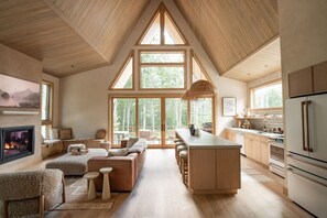 A spacious living area with a fireplace, a large window, and a kitchen with wooden cabinets.