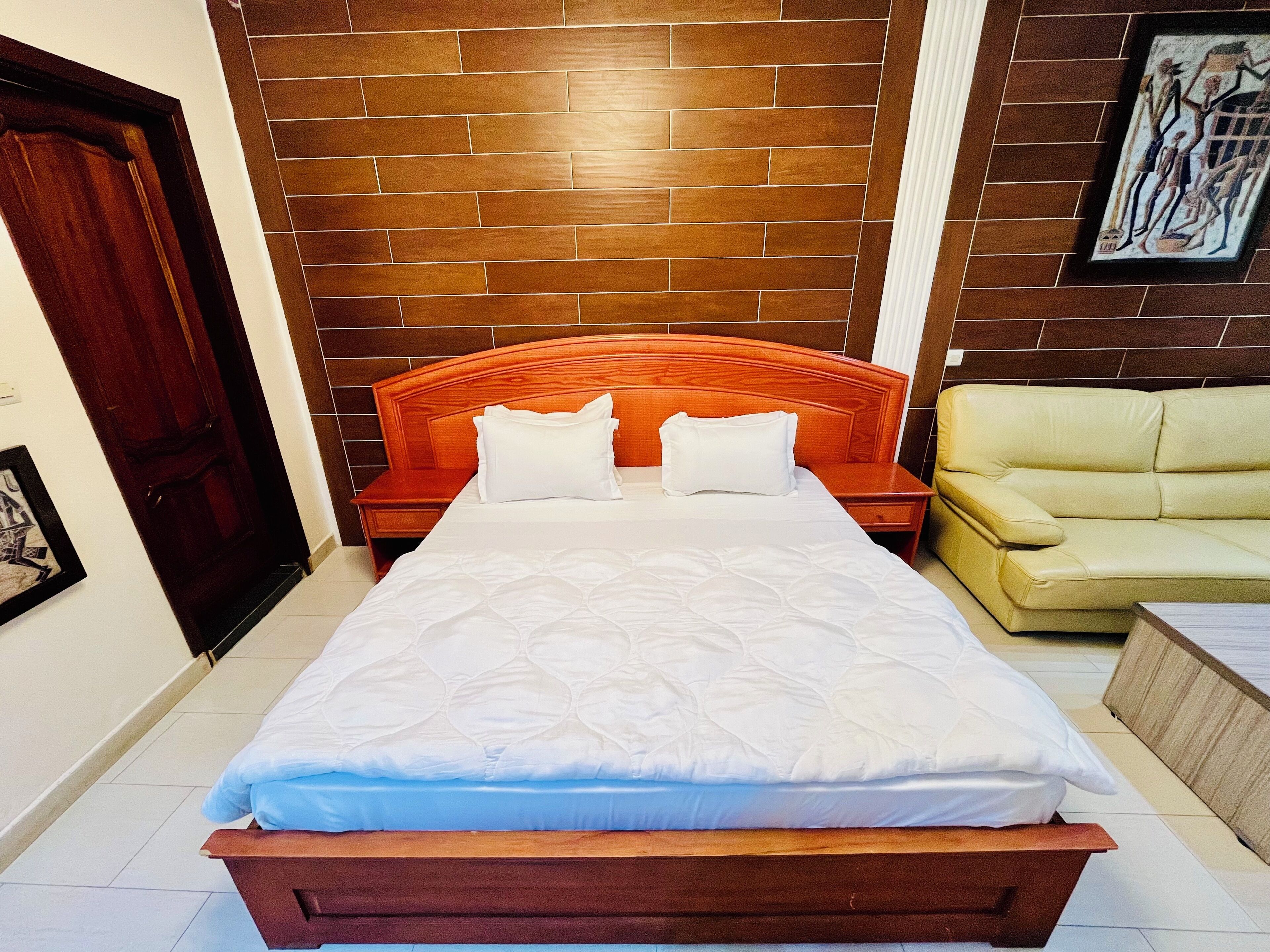 A hotel room with a wooden bed, a beige sofa, and a framed picture on the wall.