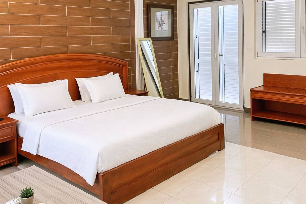 A modern bedroom with a wooden headboard bed, a bedside table with a remote, a small plant, and a nightstand.