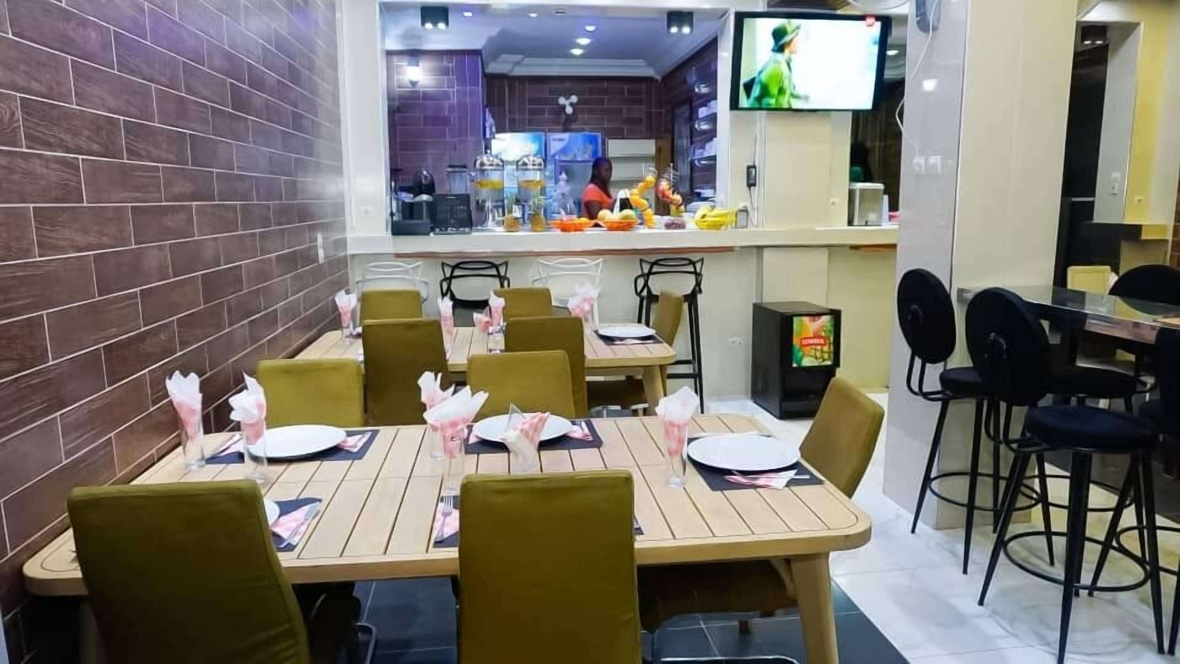 A restaurant with wooden tables and chairs, a TV screen, and a counter with food items.