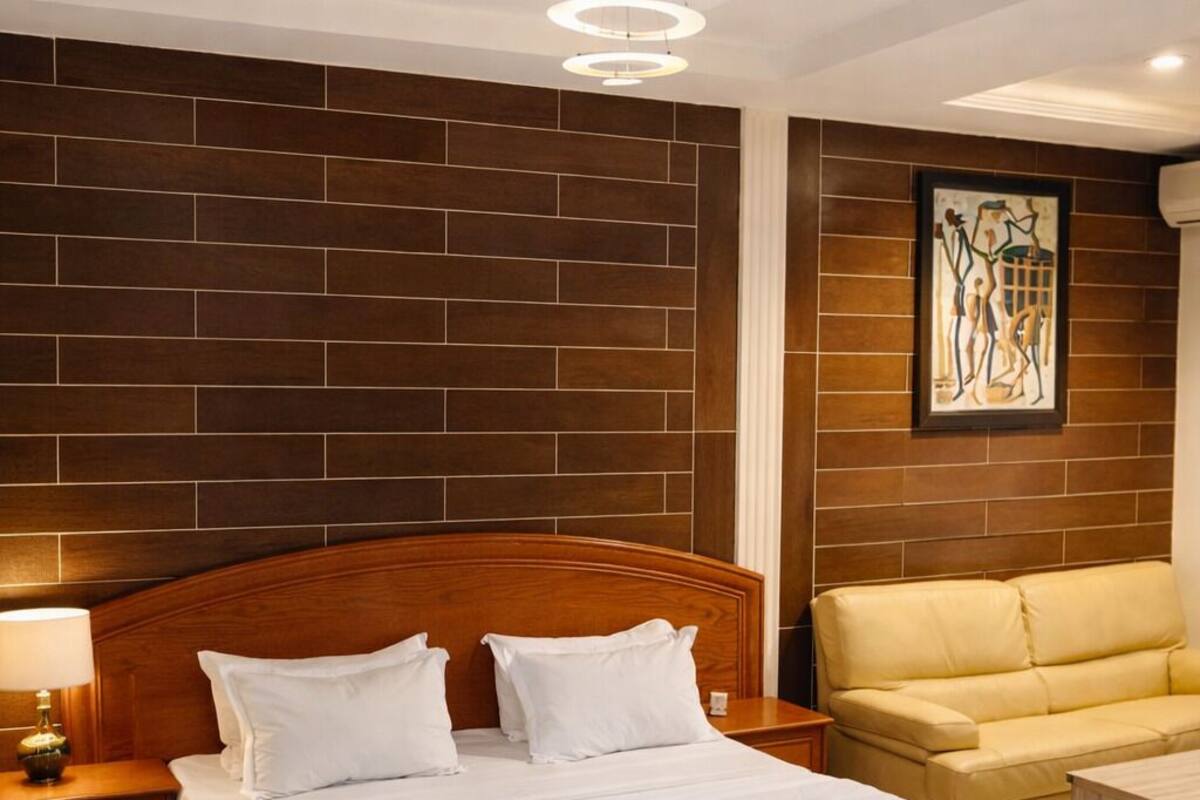 A neatly arranged hotel room with a large bed, a sofa, a coffee table, and a wall-mounted artwork.