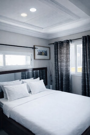 A bedroom with a bed, white bedding, a framed picture on the wall, and a window with curtains.