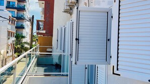Ein Balkon mit Stuhl, Glasgeländer und Blick auf benachbarte Gebäude.