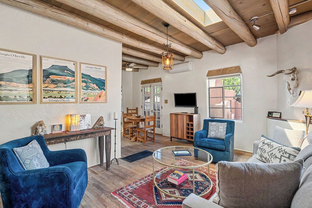 A cozy living room with a blue sofa, a glass coffee table, and a rustic ceiling.
