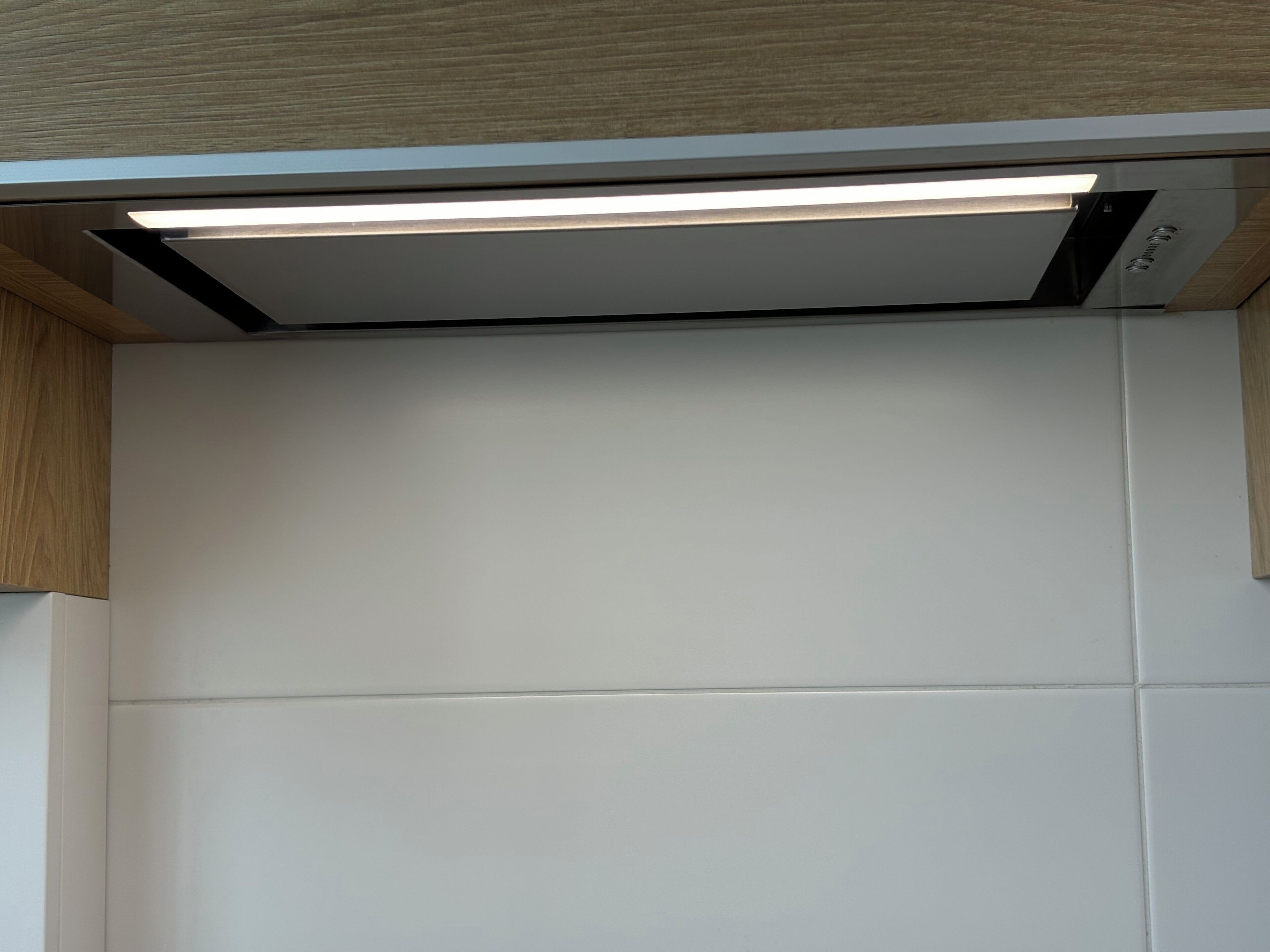 Eine moderne Küche mit weißen Schränken, einem eingebauten Backofen und einer Edelstahl-Dunstabzugshaube.