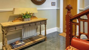 A wooden console table with a lamp and decorative items, a clock on the wall, and a staircase with a wooden railing. - Great ground floor apartment in the heart of Aberystwyth with shared hot tub. (Aberystwyth)