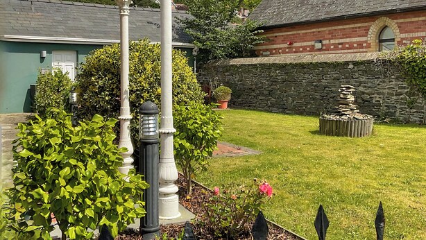 A garden with a stone wall, a white lamp post, and a brick building with a green door. - Great ground floor apartment in the heart of Aberystwyth with shared hot tub. (Aberystwyth)