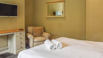 A hotel room with a bed, a desk with a chair, a television, and a mirror on the wall.