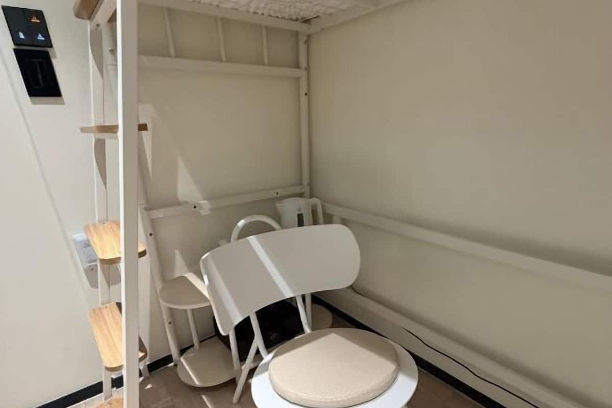 A corner of a room with a white chair, a small table, and a white shelving unit against a wall.